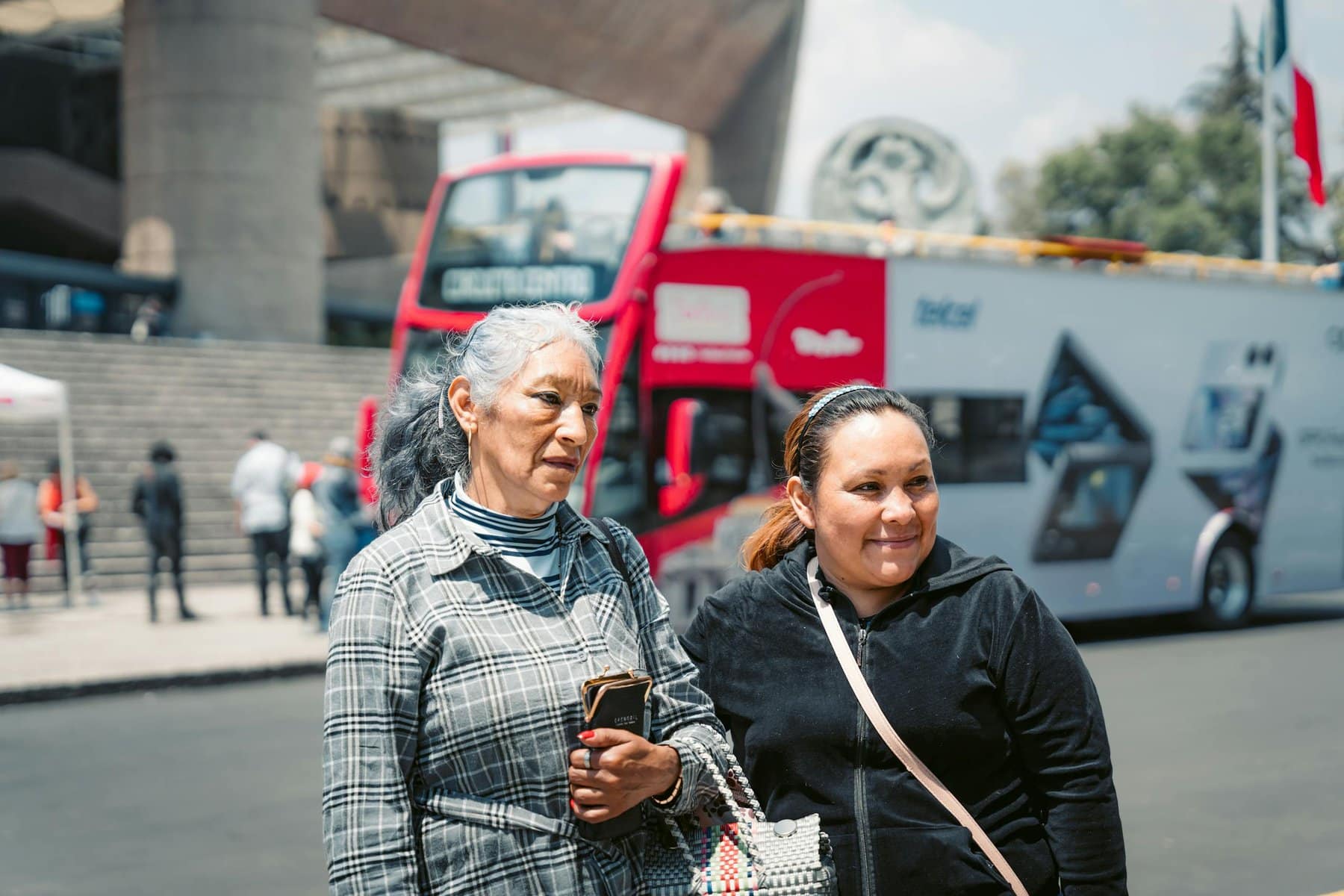 Two women posing in front of a tour bus on a busy street in Mexico City, capturing vibrant urban life.