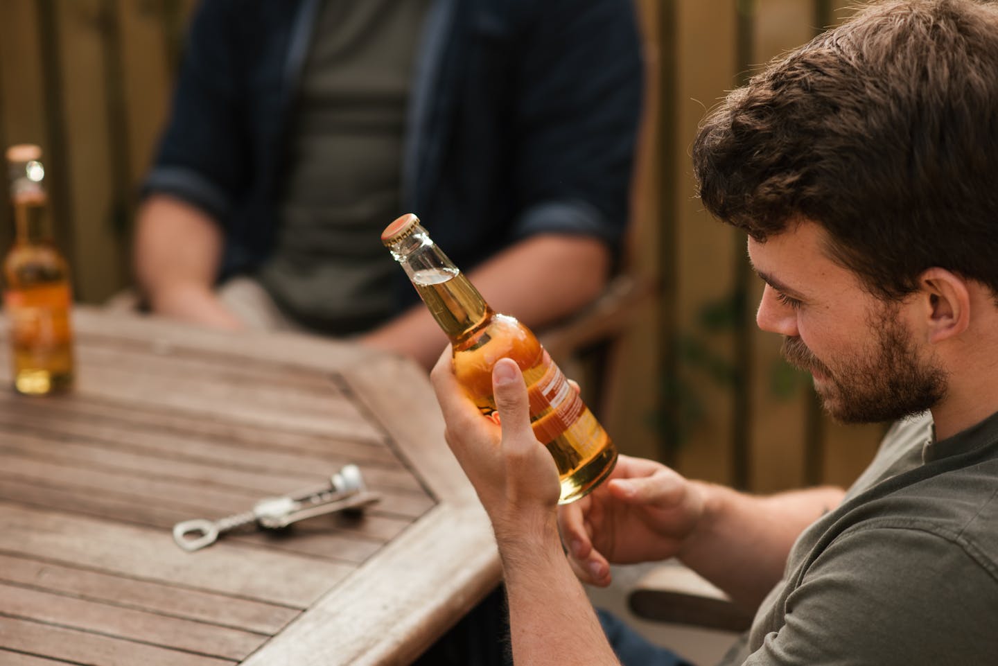 A casual moment with friends enjoying beer outdoors on a wooden terrace table.