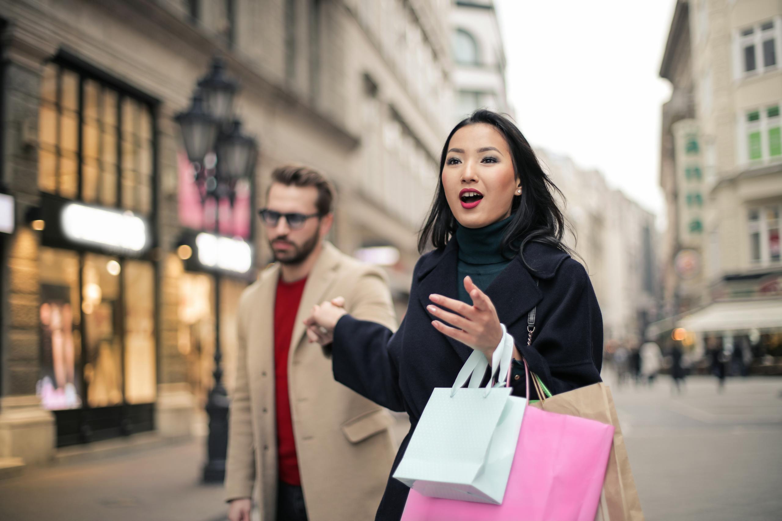 A couple enjoying a shopping day in a bustling city street, carrying colorful bags.