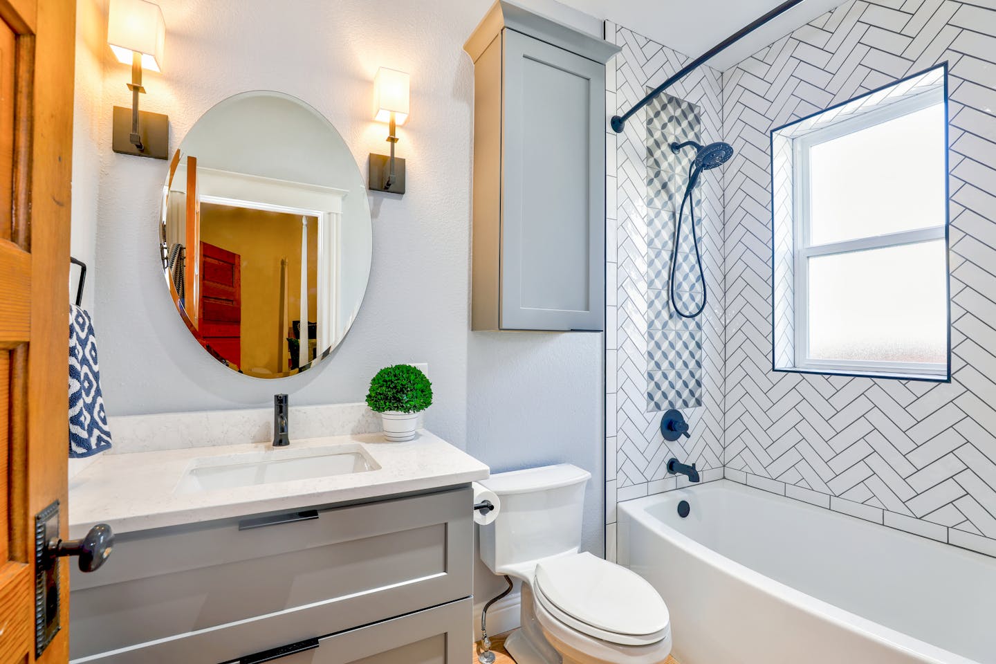 Elegant modern bathroom featuring chevron tiles, oval mirror, and sleek fixtures for a contemporary look, toilet