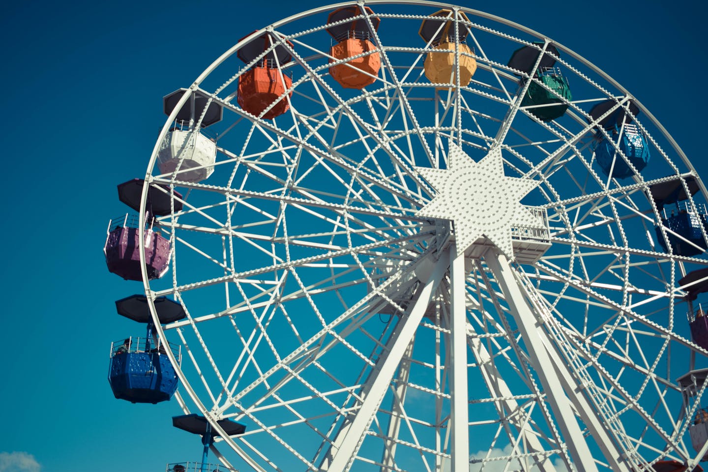 Colorful ferris wheel reaches high into a clear blue sky at a theme park, creating a fun and adventurous vibe.