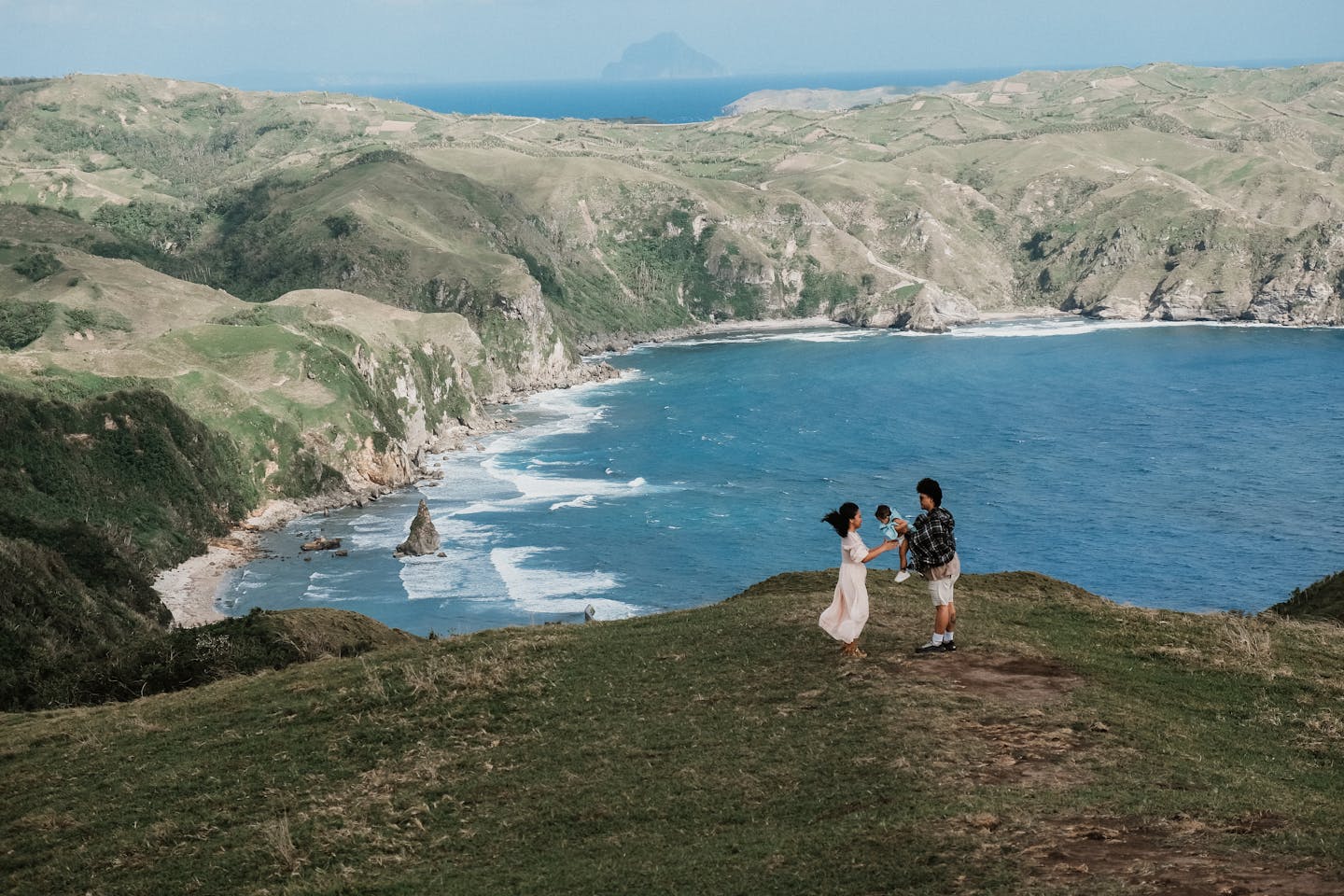 A family enjoys a stunning view of rolling hills and ocean cliffs in Batanes, Philippines.