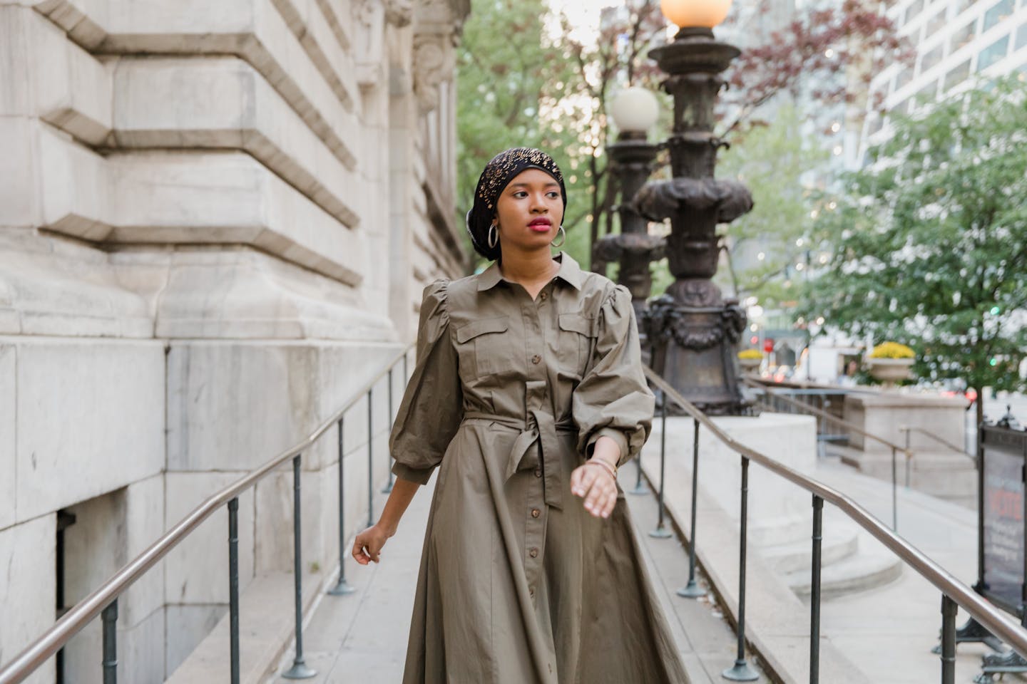 A fashionable woman in a modest outfit walking along an urban street with historical architecture.
