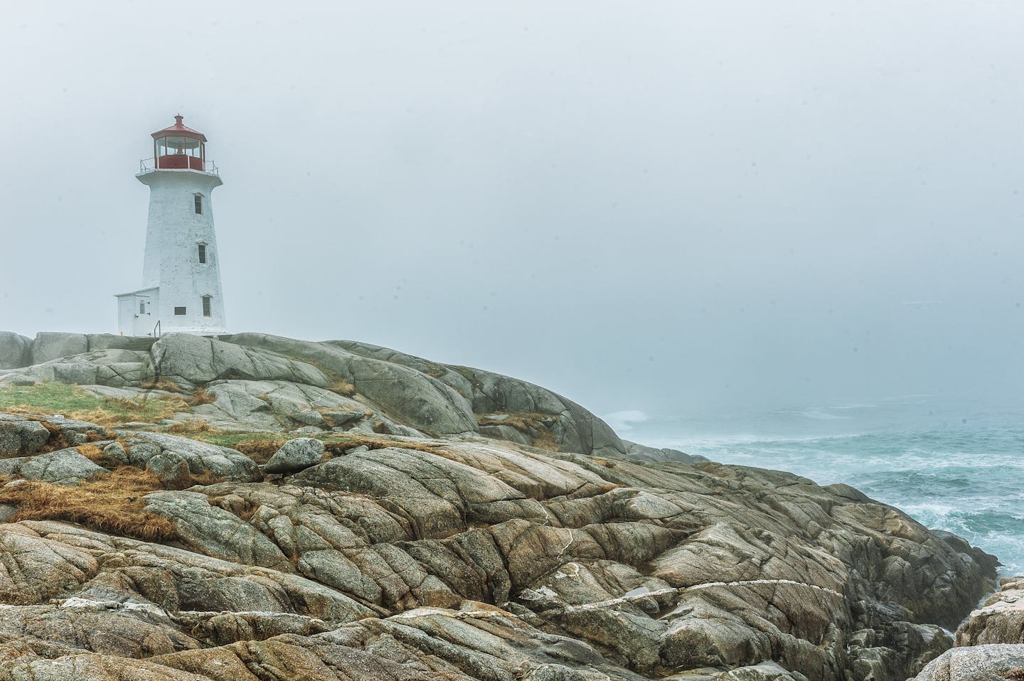 A foggy landscape with a solitary lighthouse standing on a rocky seashore during the day.