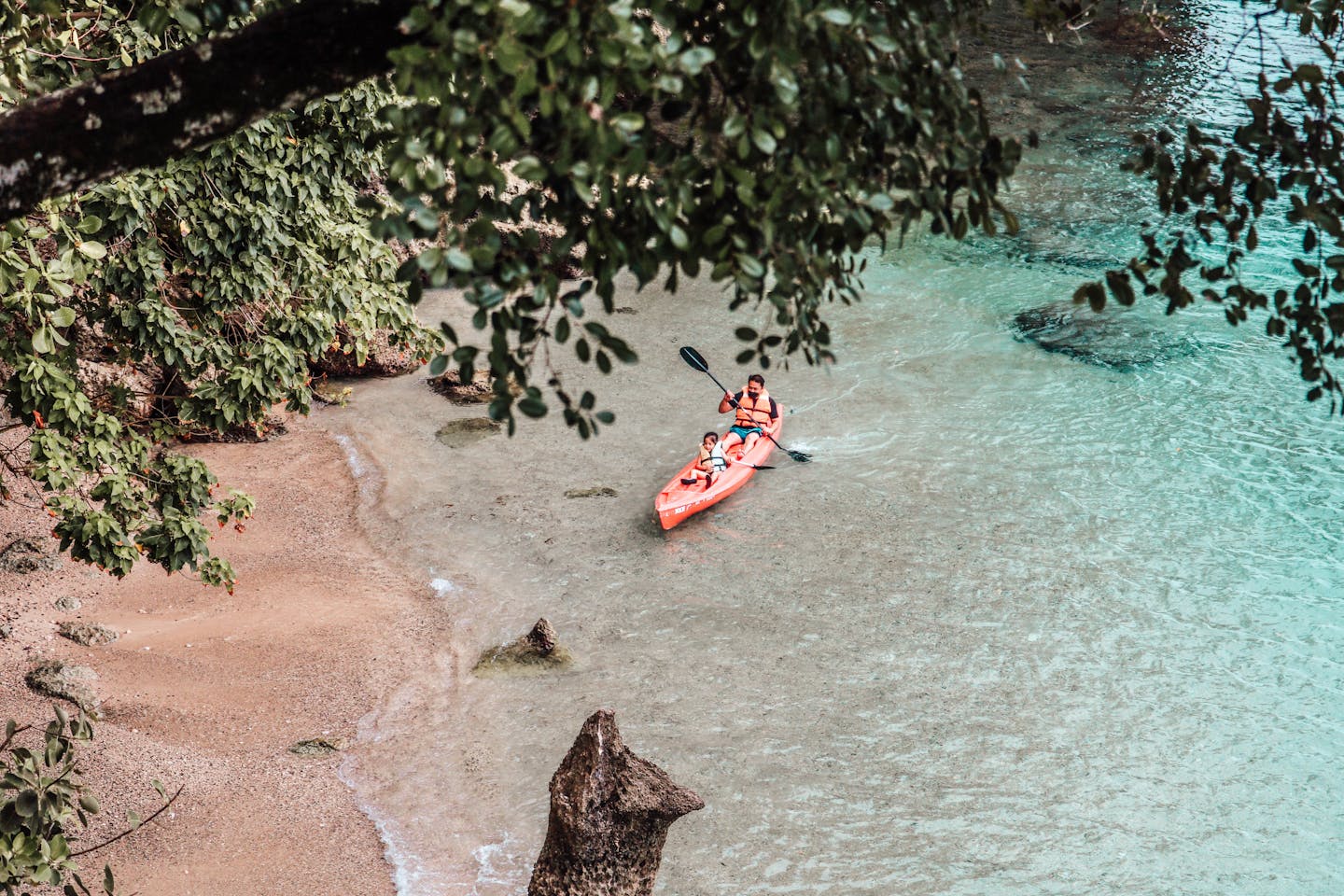 A man and child kayak through clear waters along a sandy shore in Samal Island, Philippines.