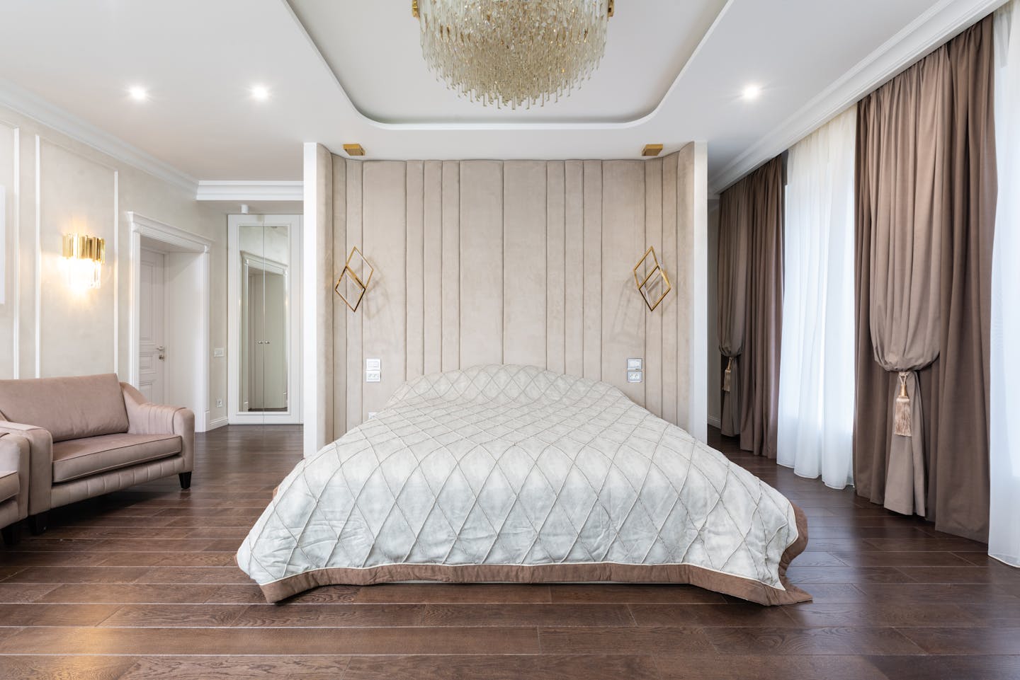 Interior of modern bedroom with bed next to armchairs under chandelier with curtains on windows