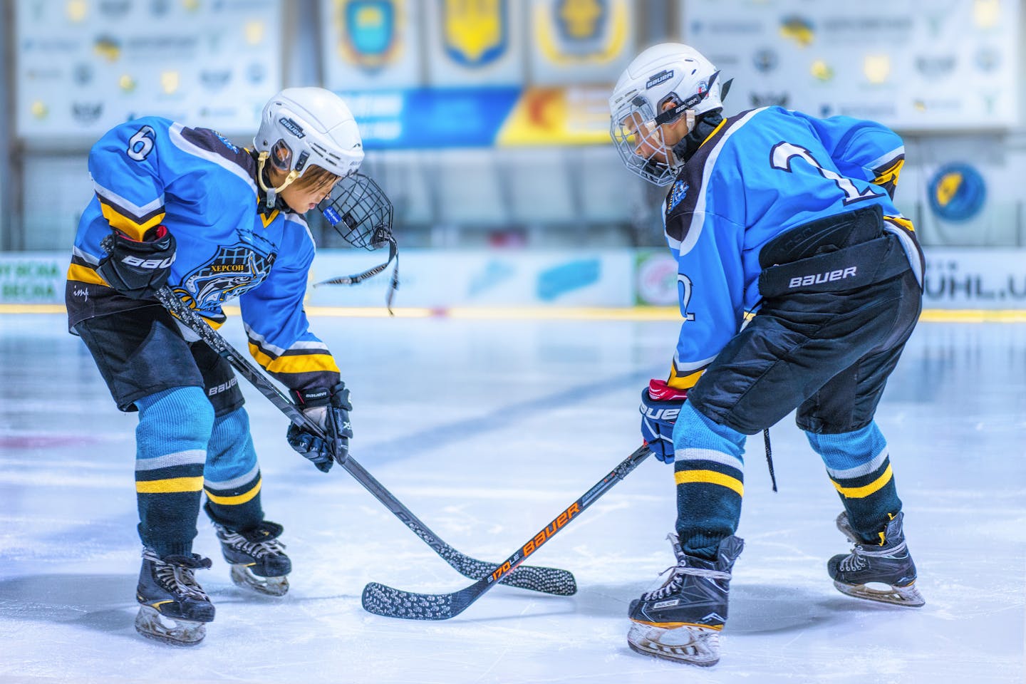 Two young athletes face-off during an ice hockey game in an indoor rink.