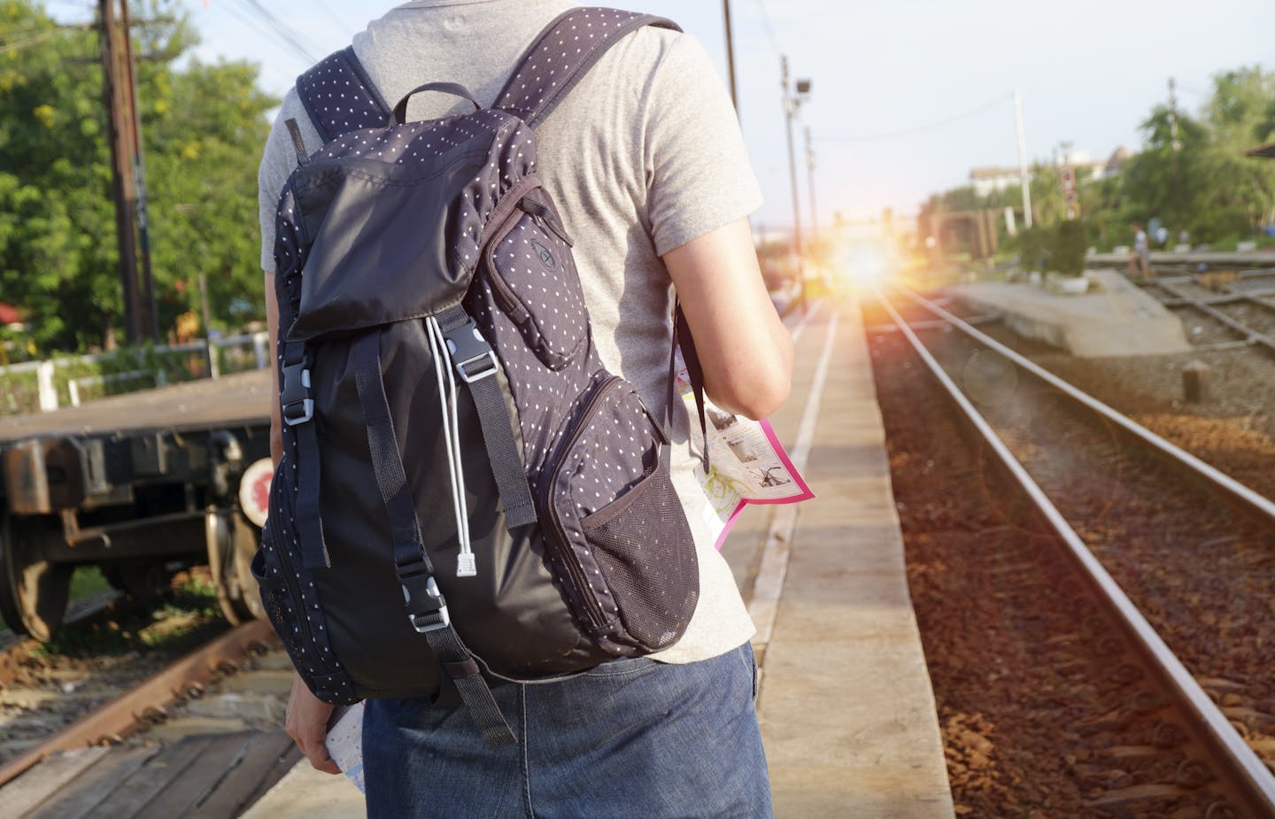 A person with a backpack waits at a railway station during daytime.