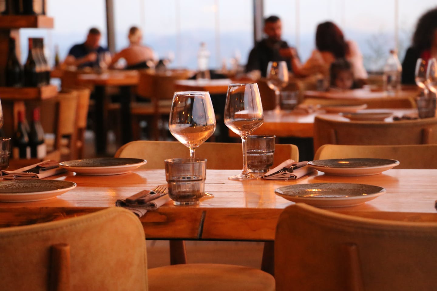 A warmly lit restaurant table set with glassware, plates, and napkins ready for a meal.