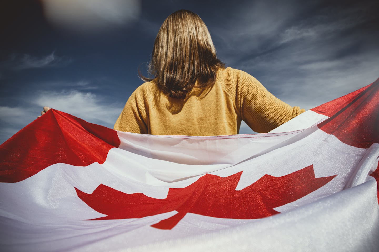 A woman holding the Canadian flag with mountains in Banff, Alberta, Canada.