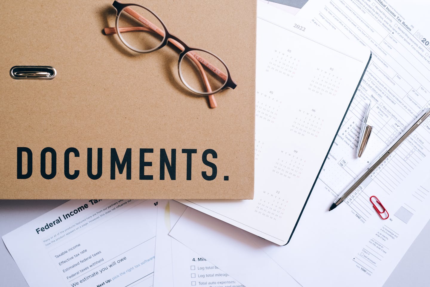 Flat lay of office supplies including documents, calendar, and eyeglasses on a desk.