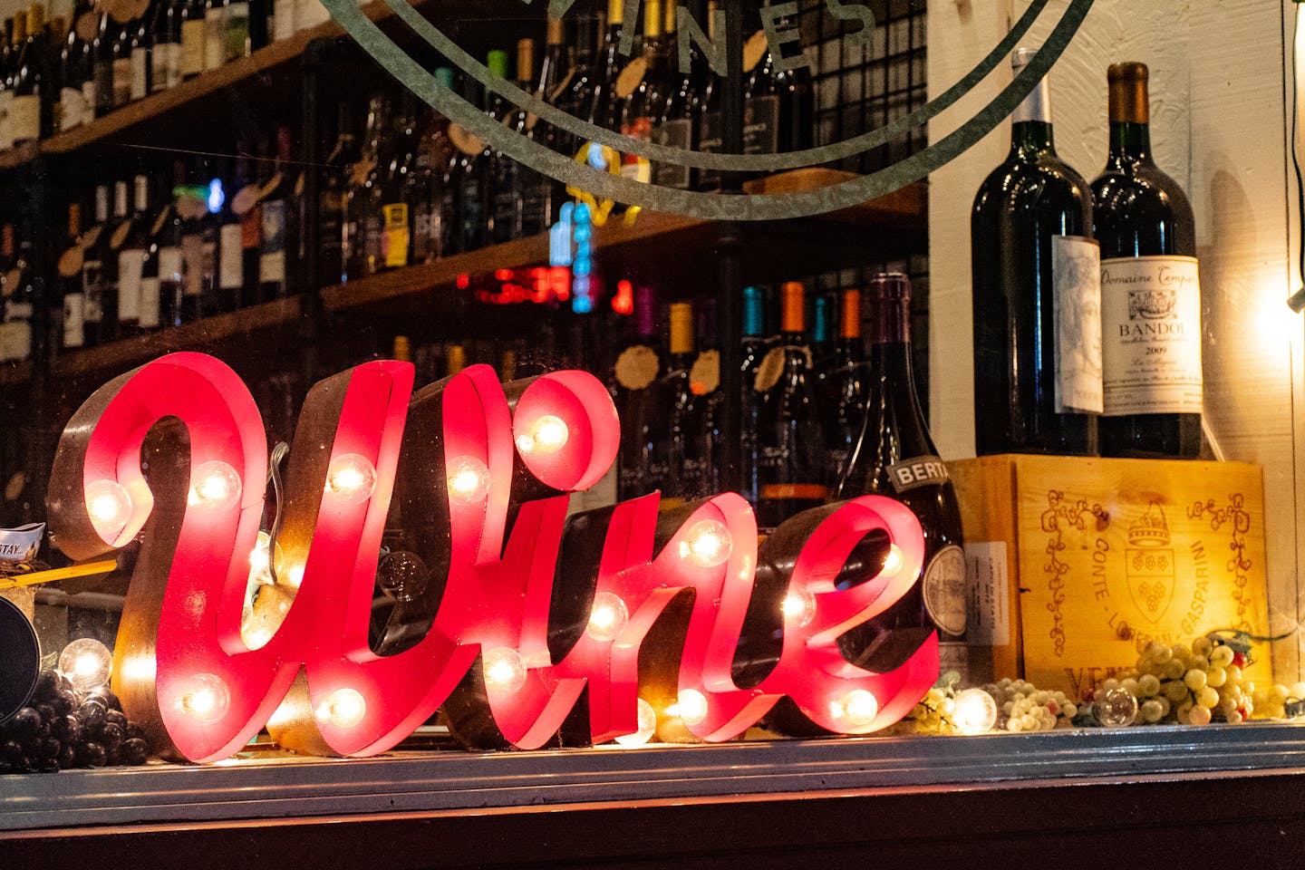Illuminated wine sign with bottles and grapes create a lively ambiance in a liquor store window.