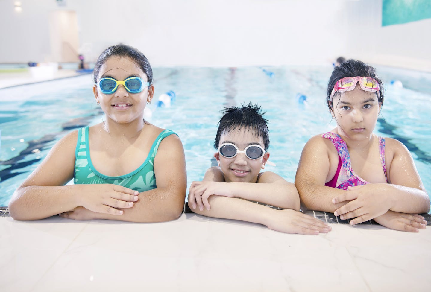 Three smiling children in swimwear enjoying a swim at an indoor pool. Perfect for lifestyle and leisure themes.
