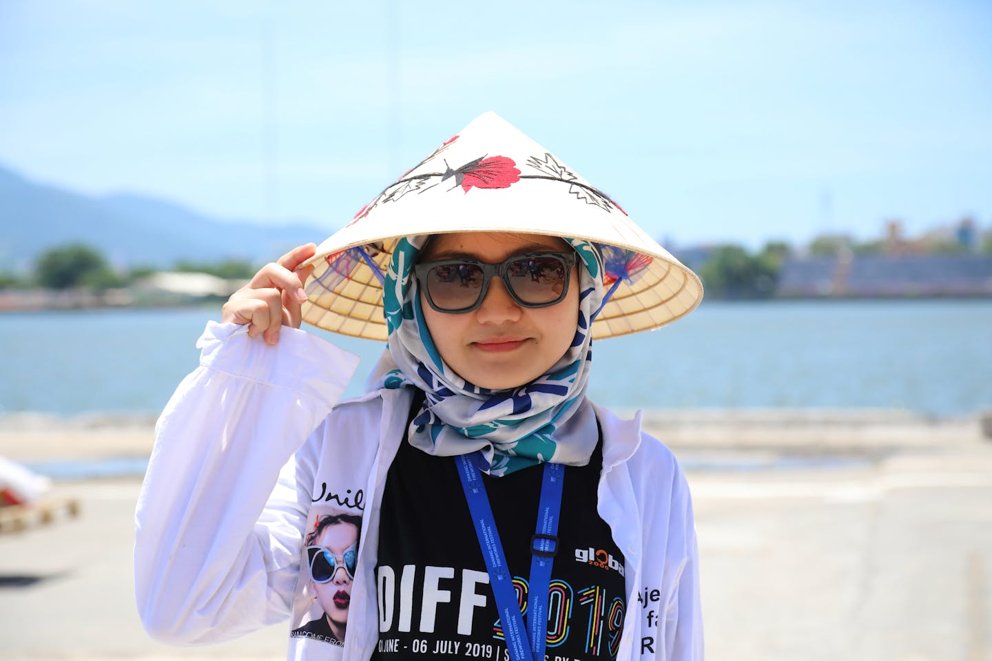 A woman in an Asian conical hat by the water, embracing cultural style.