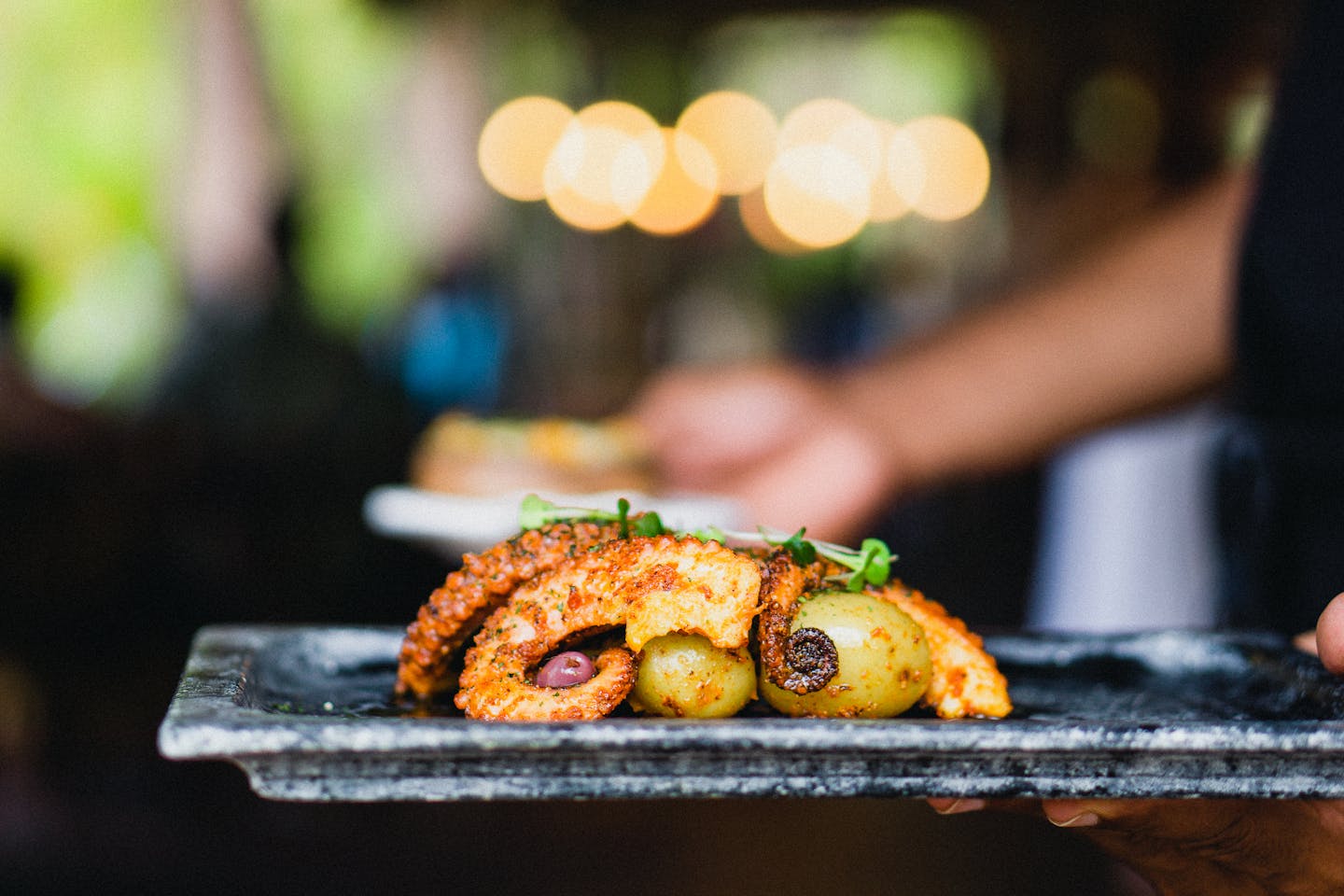 Close-up of grilled octopus elegantly plated with olives, featuring a blurred background.