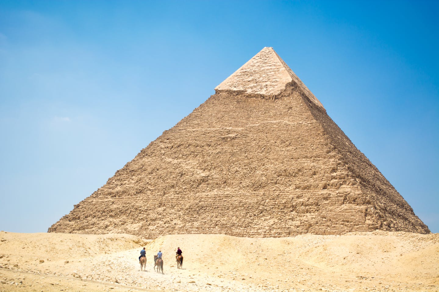 Iconic Giza Pyramid with riders on camels under bright daylight, capturing Egyptian desert landscapes.