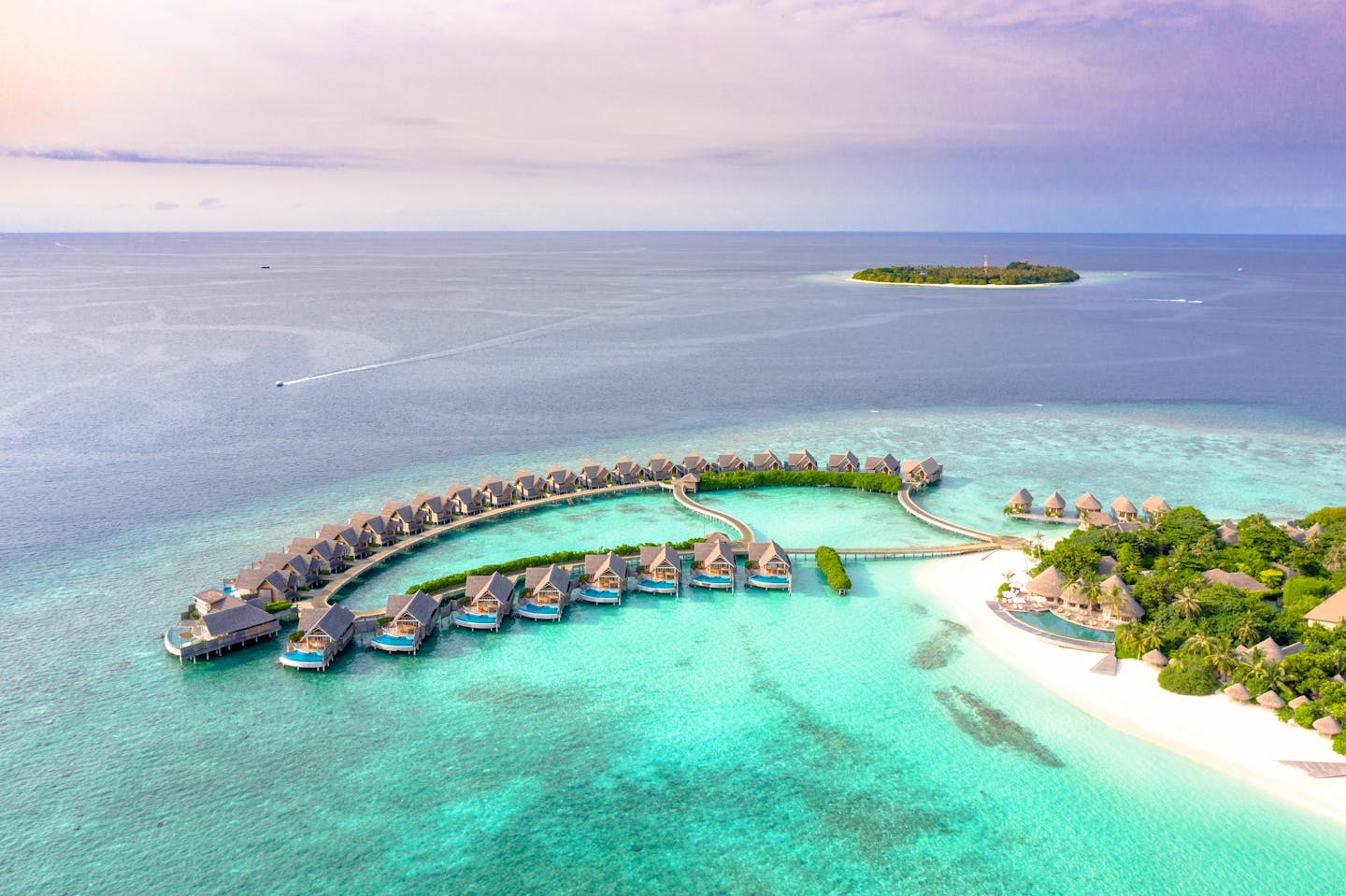 Idyllic aerial view of luxury overwater villas on a tropical island's crystal-clear waters.