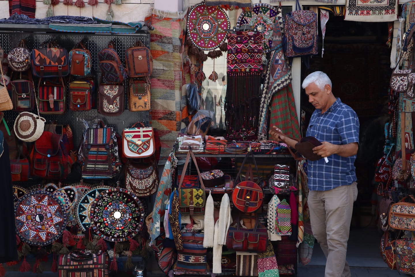 Man exploring traditional Turkish market with vibrant artisanal bags and textiles.