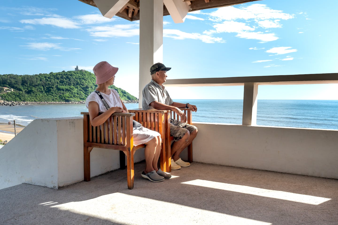 Senior couple sitting on balcony chairs, enjoying a relaxing ocean view in summer.