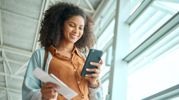 Black woman at airport, travel with smartphone and plane ticket, communication and check social media with smile. Notification, email or chat with technology, ready for flight and happy for adventure