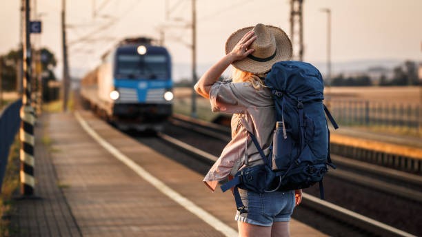 Woman backpacker with hat standing at railroad station and looking to arriving train